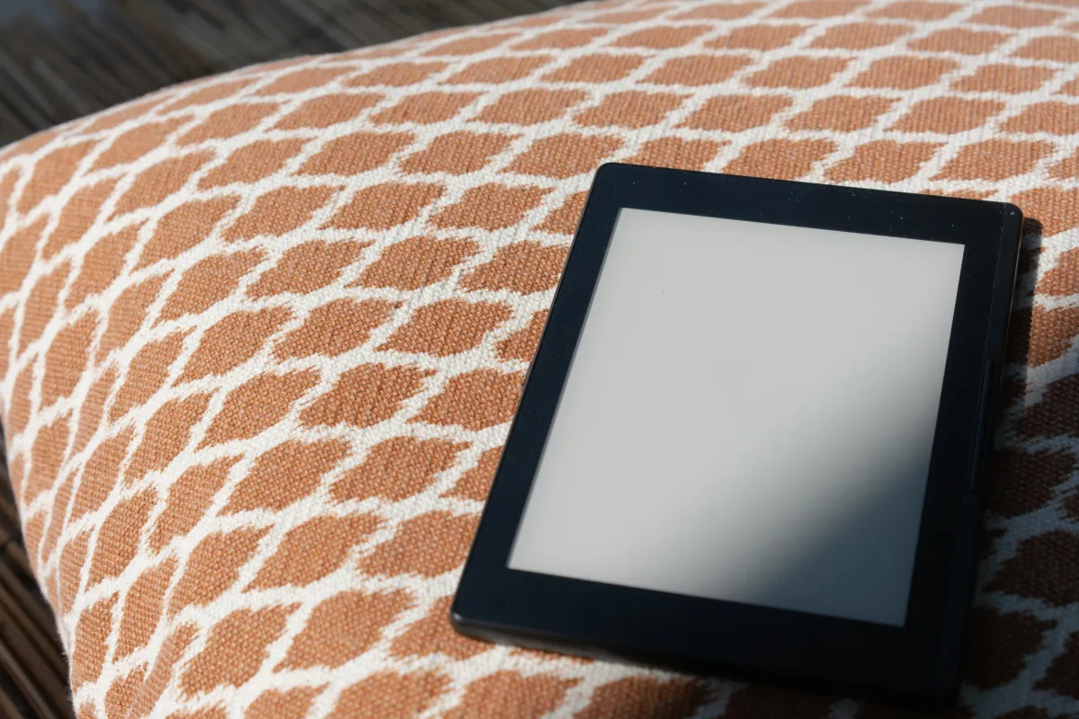 Leitor digital (e-reader) com tela desligada sobre almofada com estampa geométrica em tons laranja e branco.