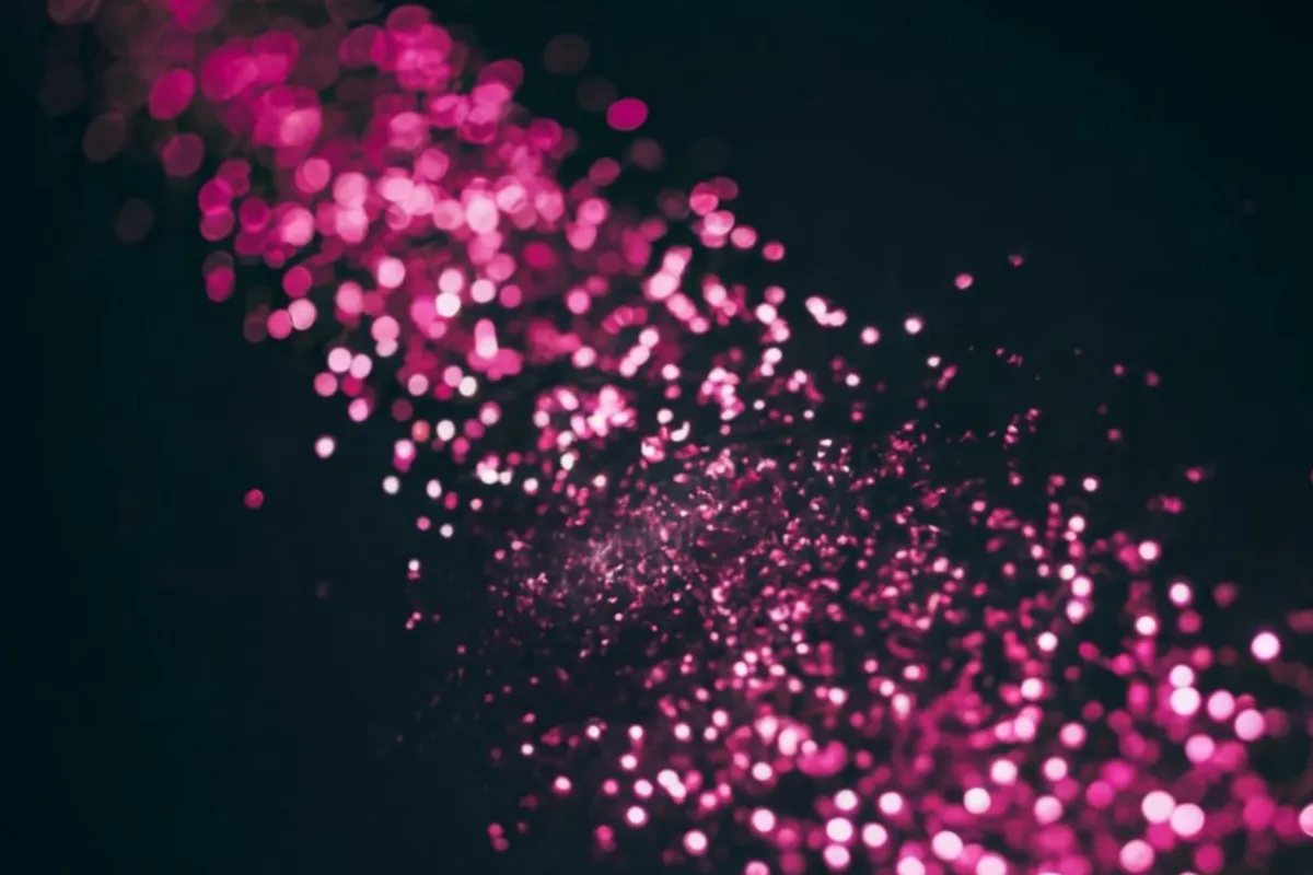 Partículas rosa brilhantes em efeito bokeh sobre fundo preto e desfocado