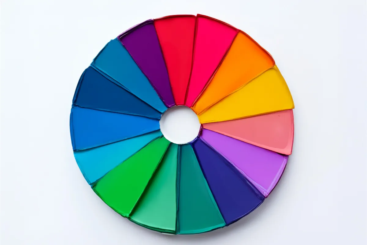 Roda formada por pinceladas de tinta em cores vibrantes do espectro, dispostas em círculo com centro vazio sobre um fundo branco liso.