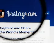 Tela com o logotipo clássico do Instagram e slogan “Capture and Share the World’s Moments”, ampliado por uma lupa em fundo azul.