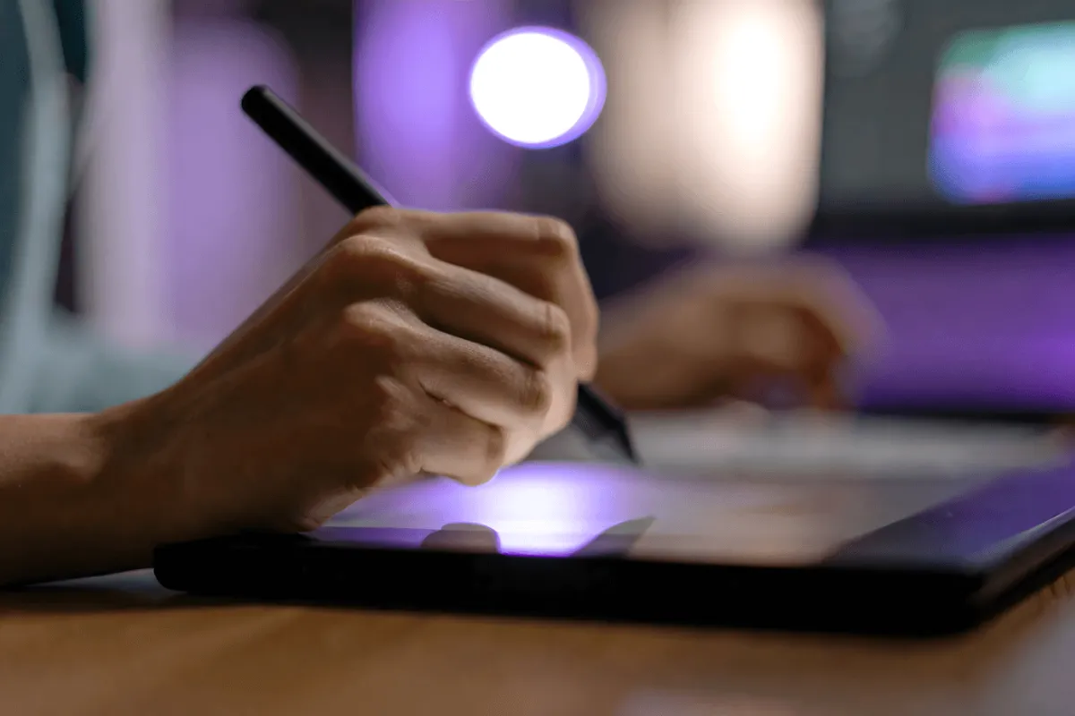 Pessoa usando caneta digital em tablet gráfico para criar design em ambiente iluminado